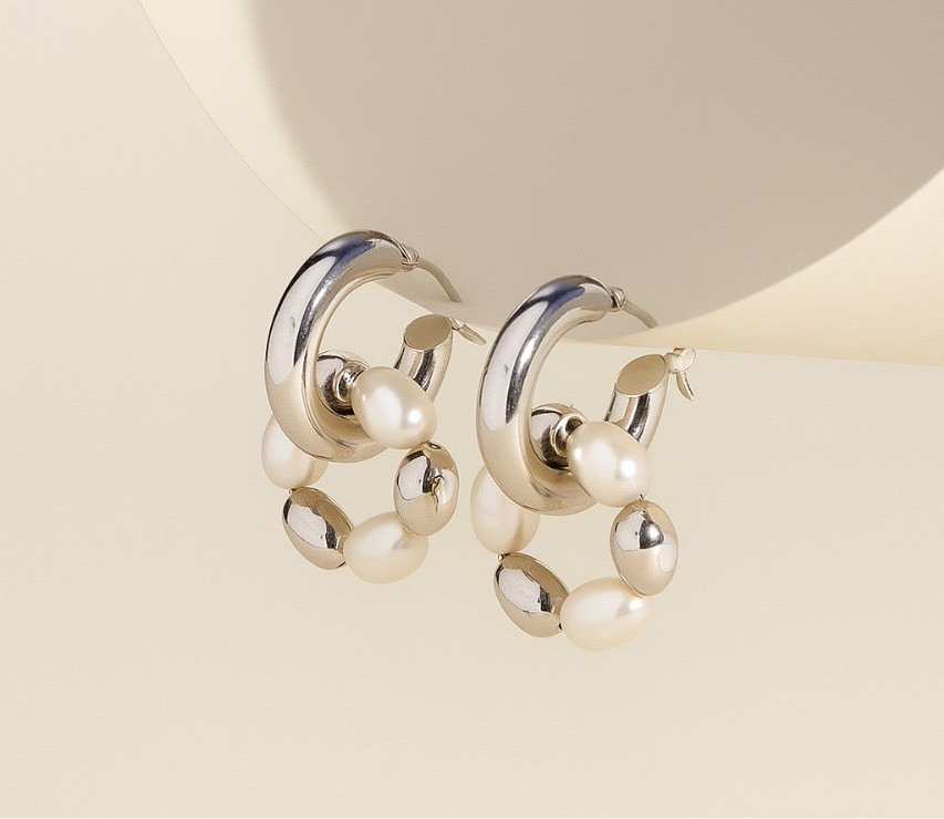 Pair of pearl and silver hoop earrings with pearls on a beige background