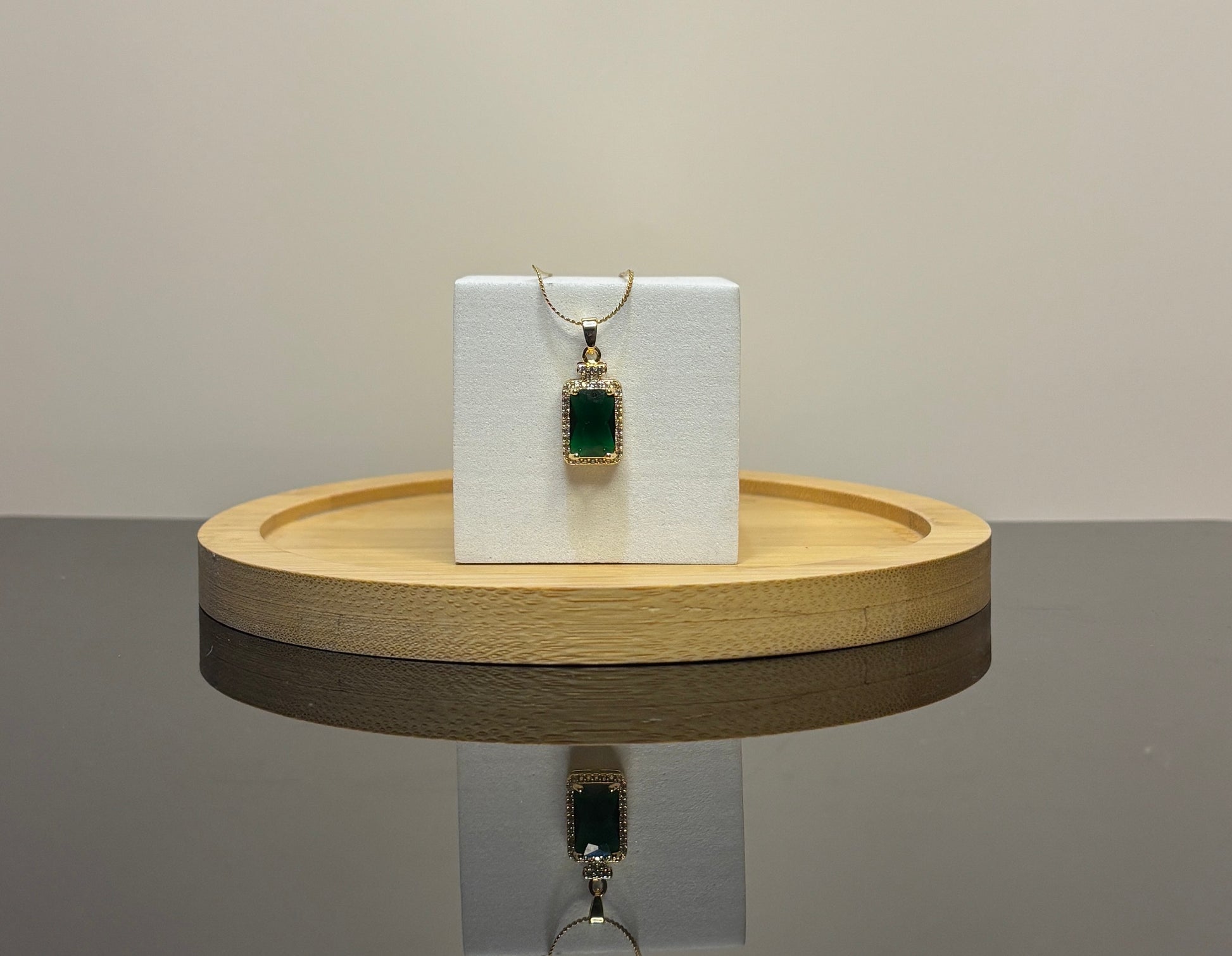 green  pendant on a white card with a wooden stand against a neutral background