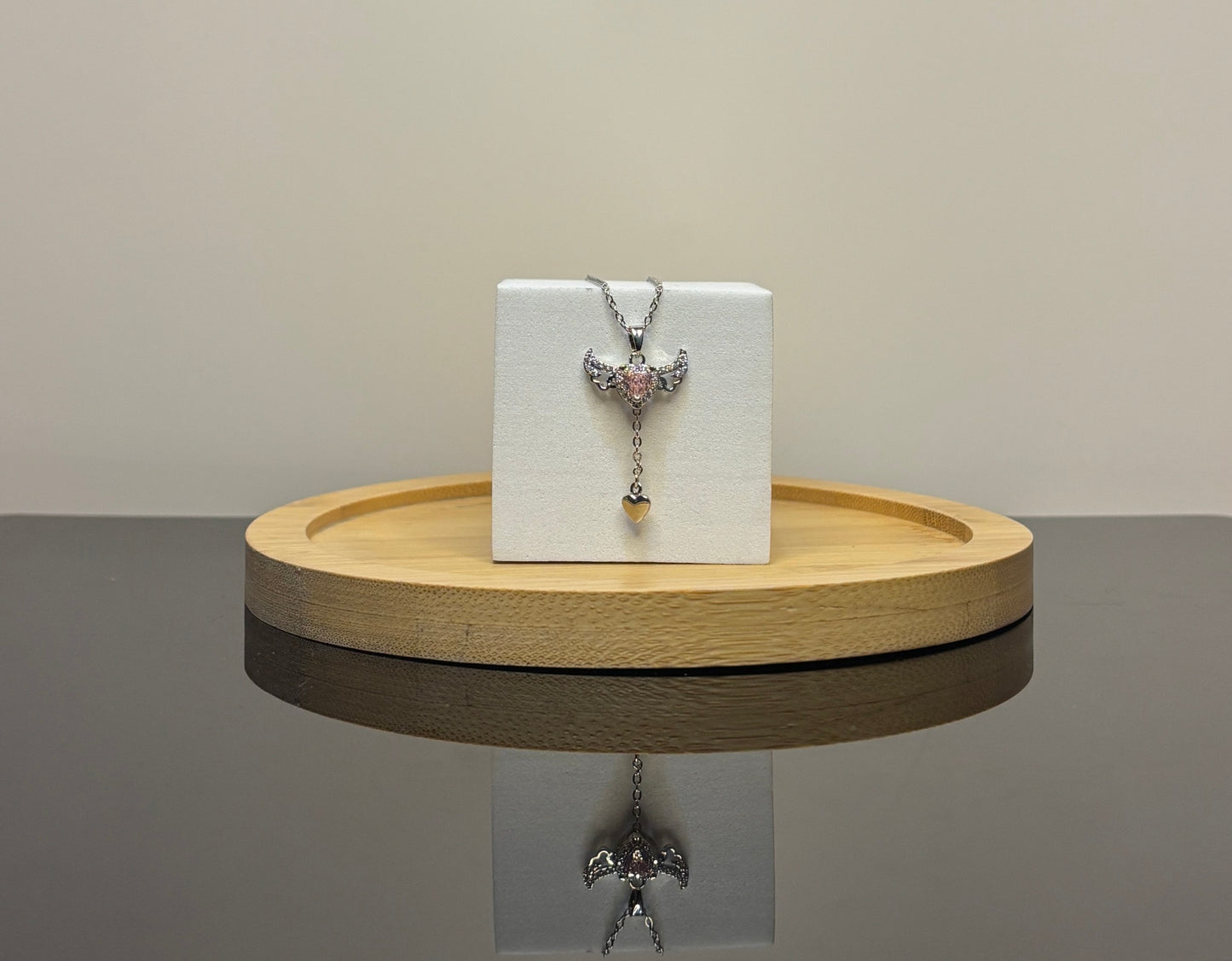 angel wings Silver necklace with a pendant on a white box on a wooden stand.