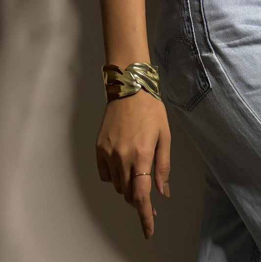Hand wearing a gold bracelet with a neutral background