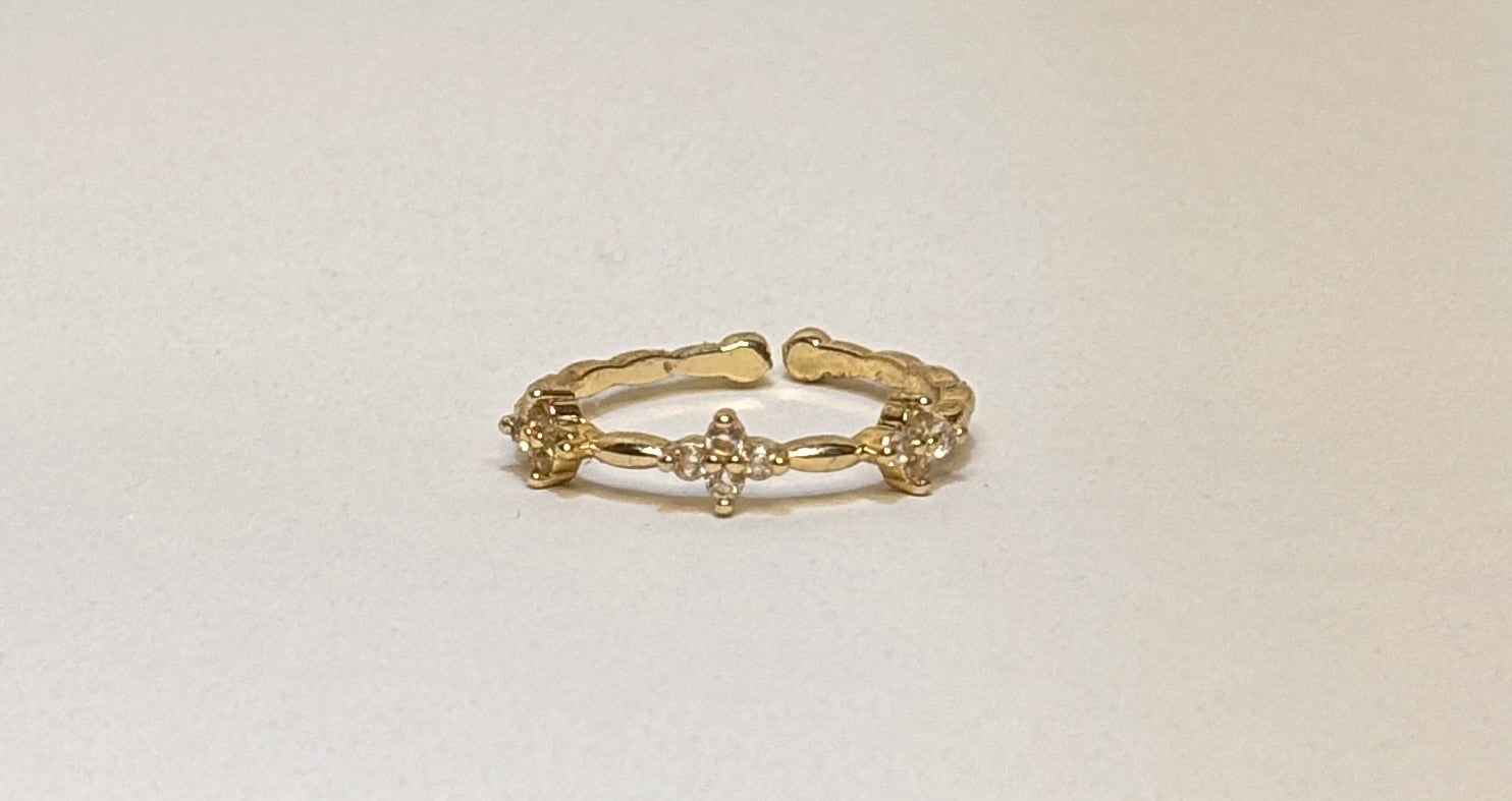 Gold ring with clover design on a light beige background