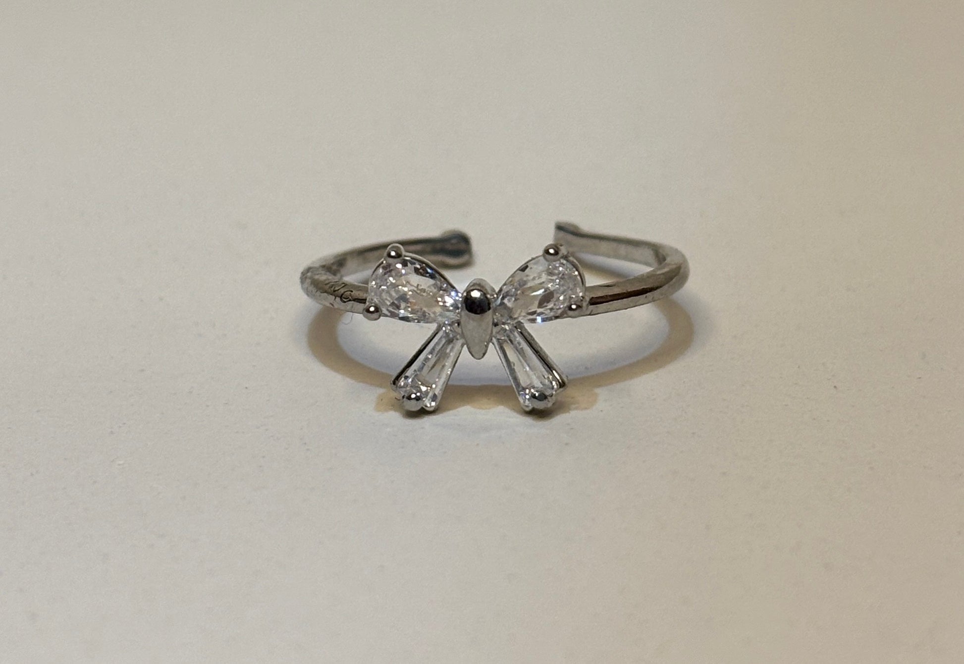 Silver bow-shaped ring with clear gemstones on a light gray background