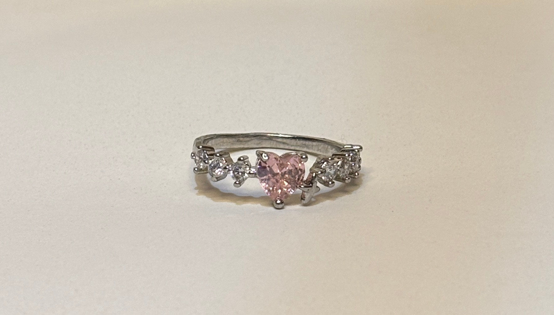 Silver ring with a pink heart-shaped gemstone on a beige background