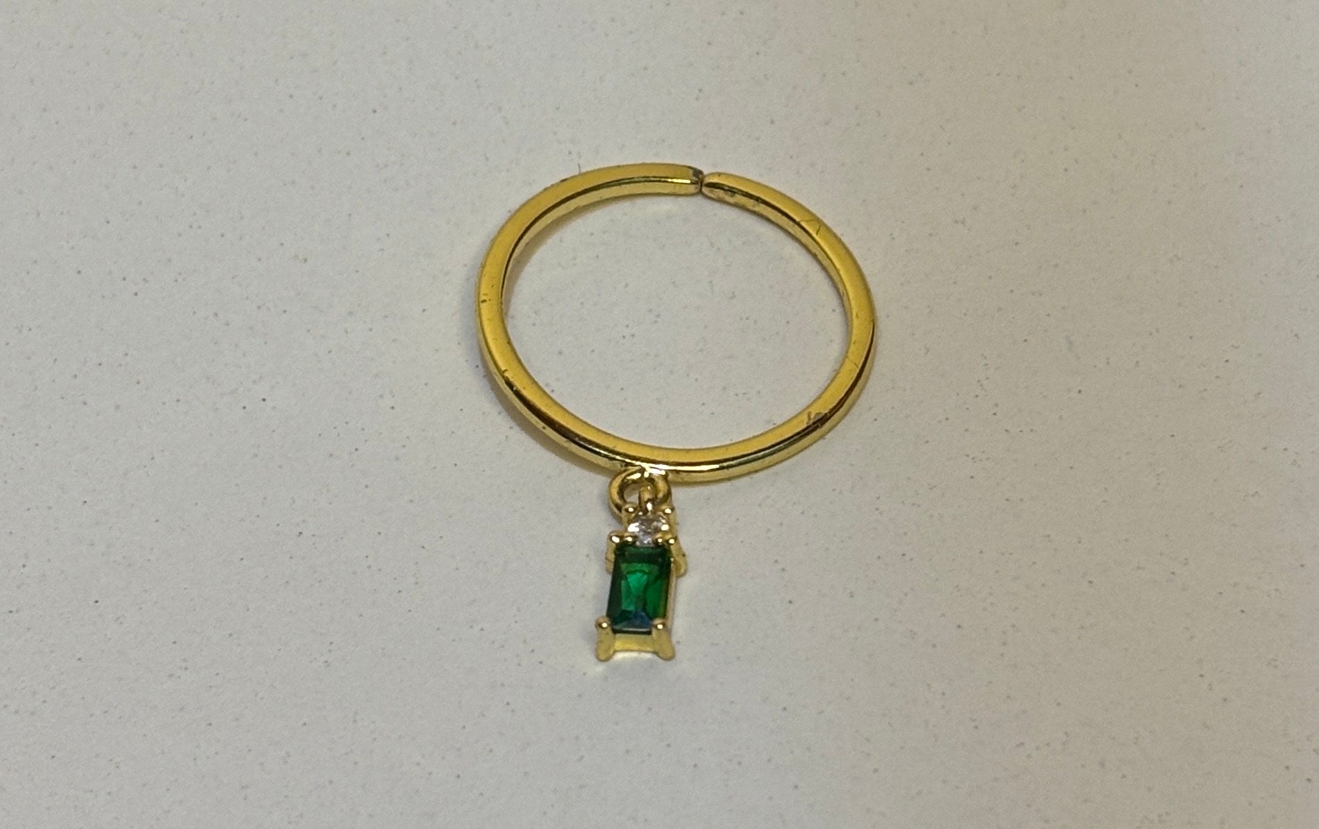 Gold ring with a green gemstone on a light gray background