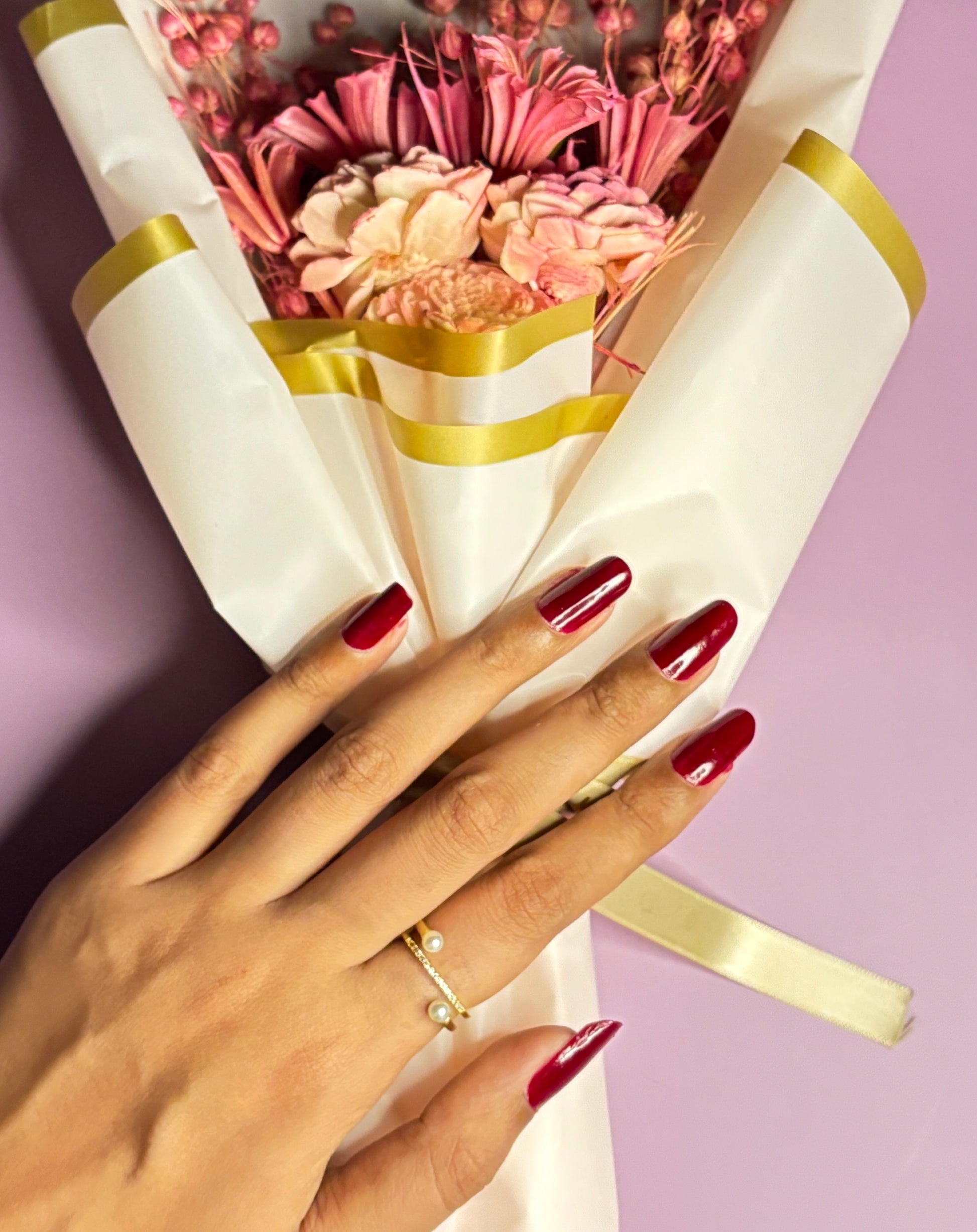 Hand holding a bouquet of flowers wrapped in white paper with gold ribbons against a purple background