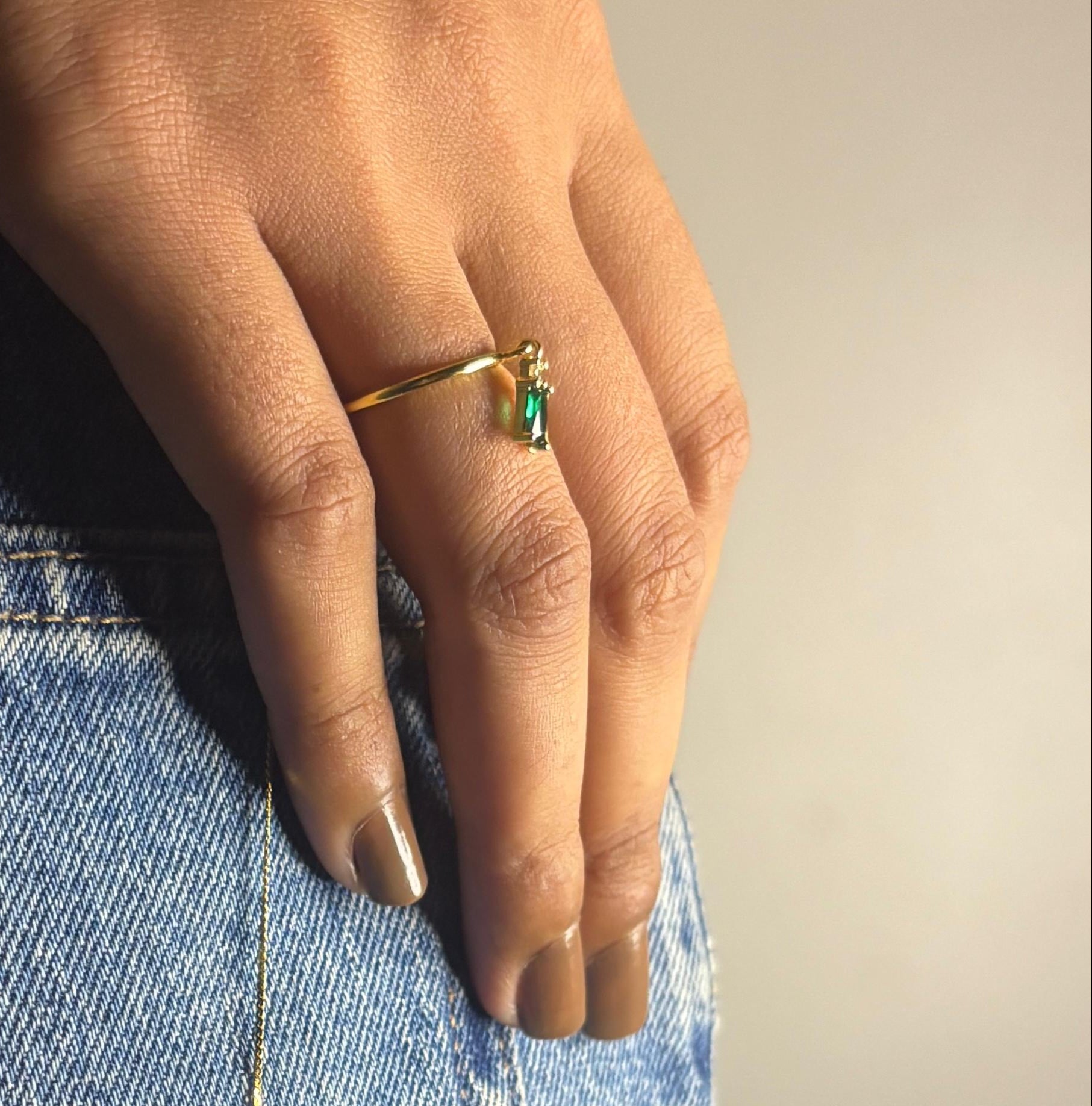 Gold necklace with a green pendant worn by a person against a denim background