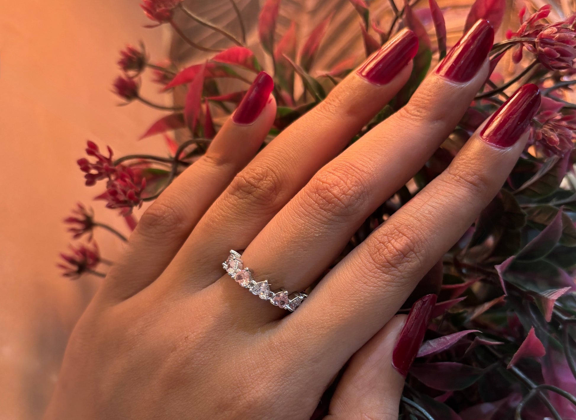 Hand wearing a heart diamond ring with red nail polish against a floral background