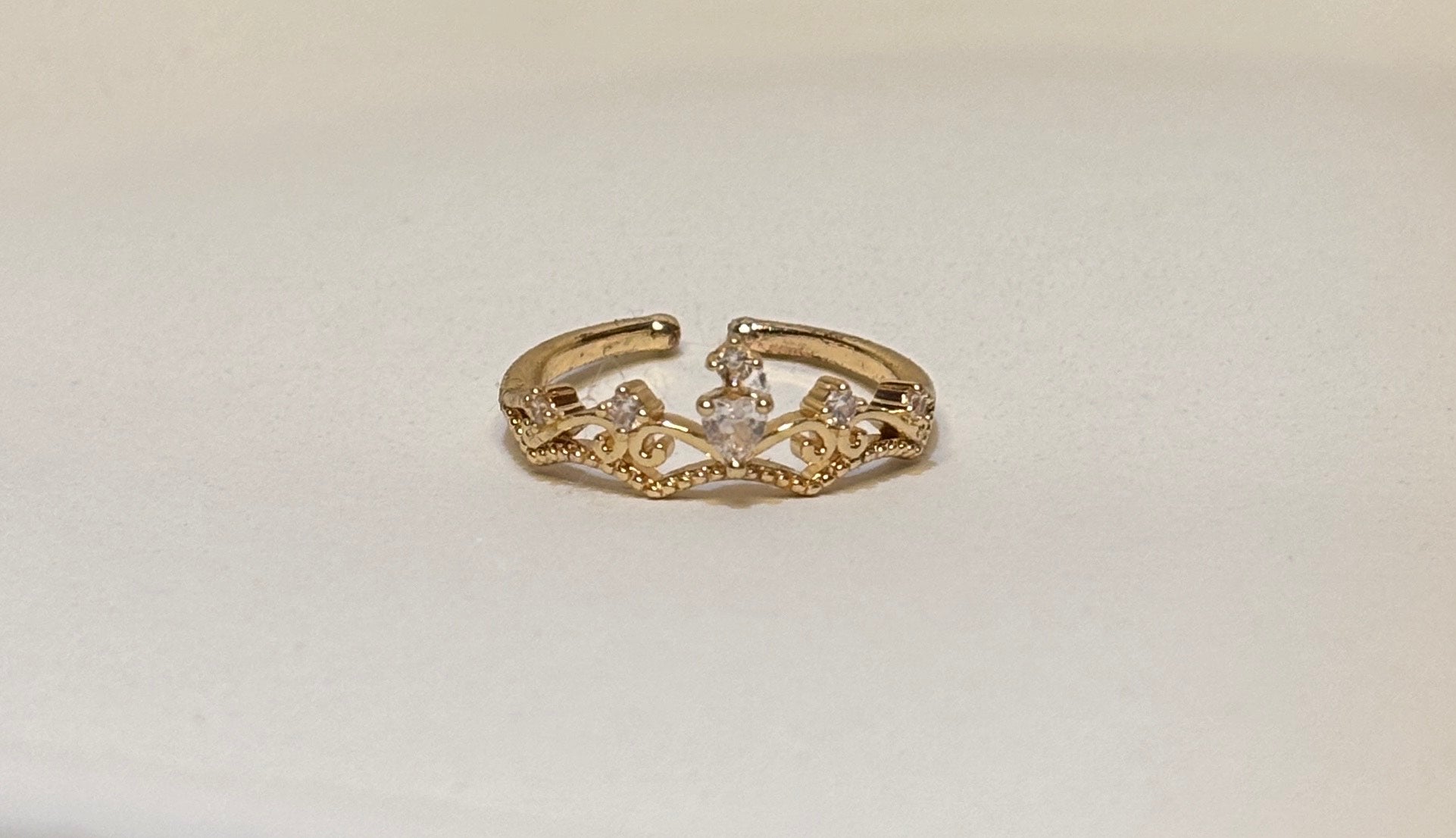 Gold ring with intricate crown design on a light gray background