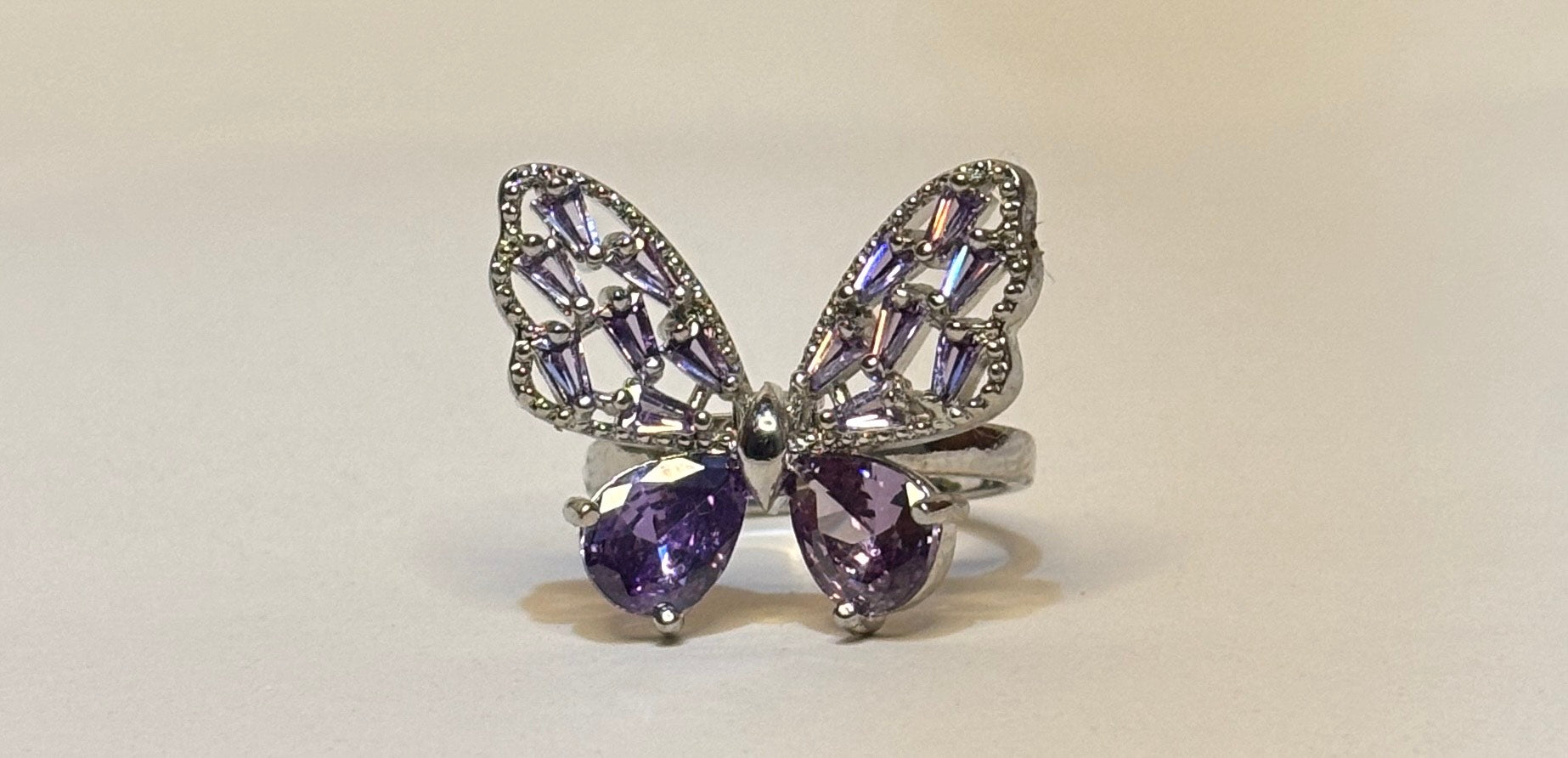 Butterfly-shaped ring with purple gemstones on a beige background