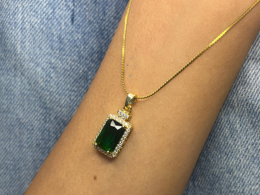 Gold necklace with a green gemstone pendant on a person's wrist against a denim background