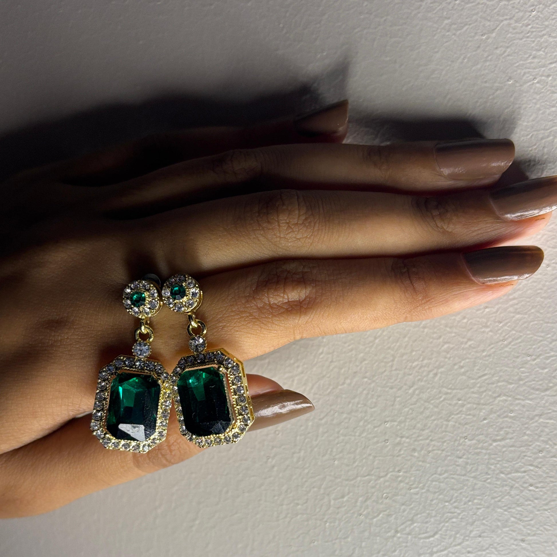 Green gemstone earrings held by a hand against a plain background