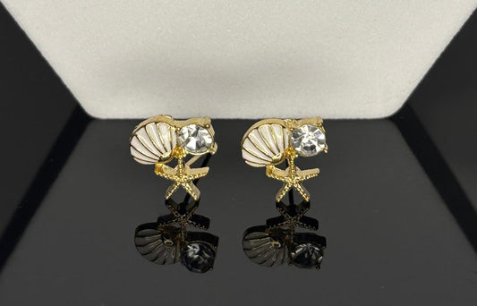 Pair of earrings with shell and starfish design on a reflective surface.