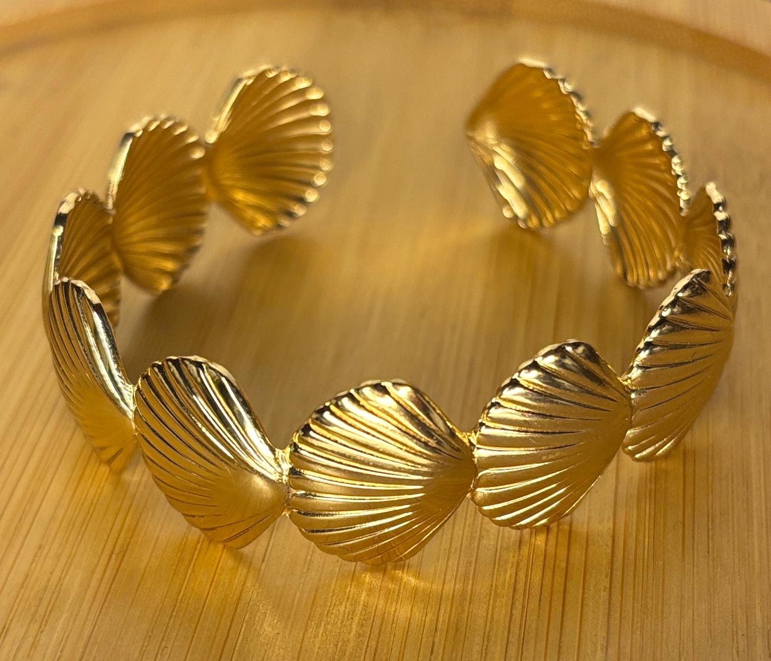 Gold bracelet with shell-like designs on a wooden surface