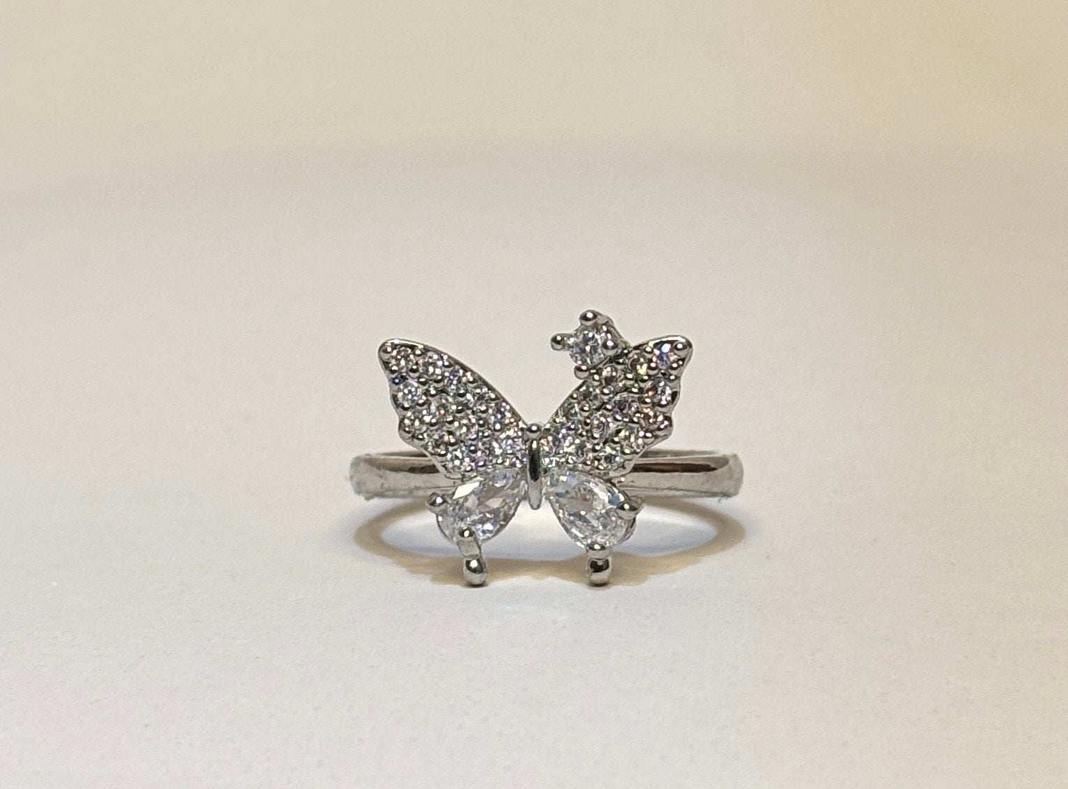 Butterfly-shaped ring with gemstones on a light beige background