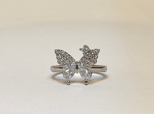 Butterfly-shaped ring with gemstones on a light beige background