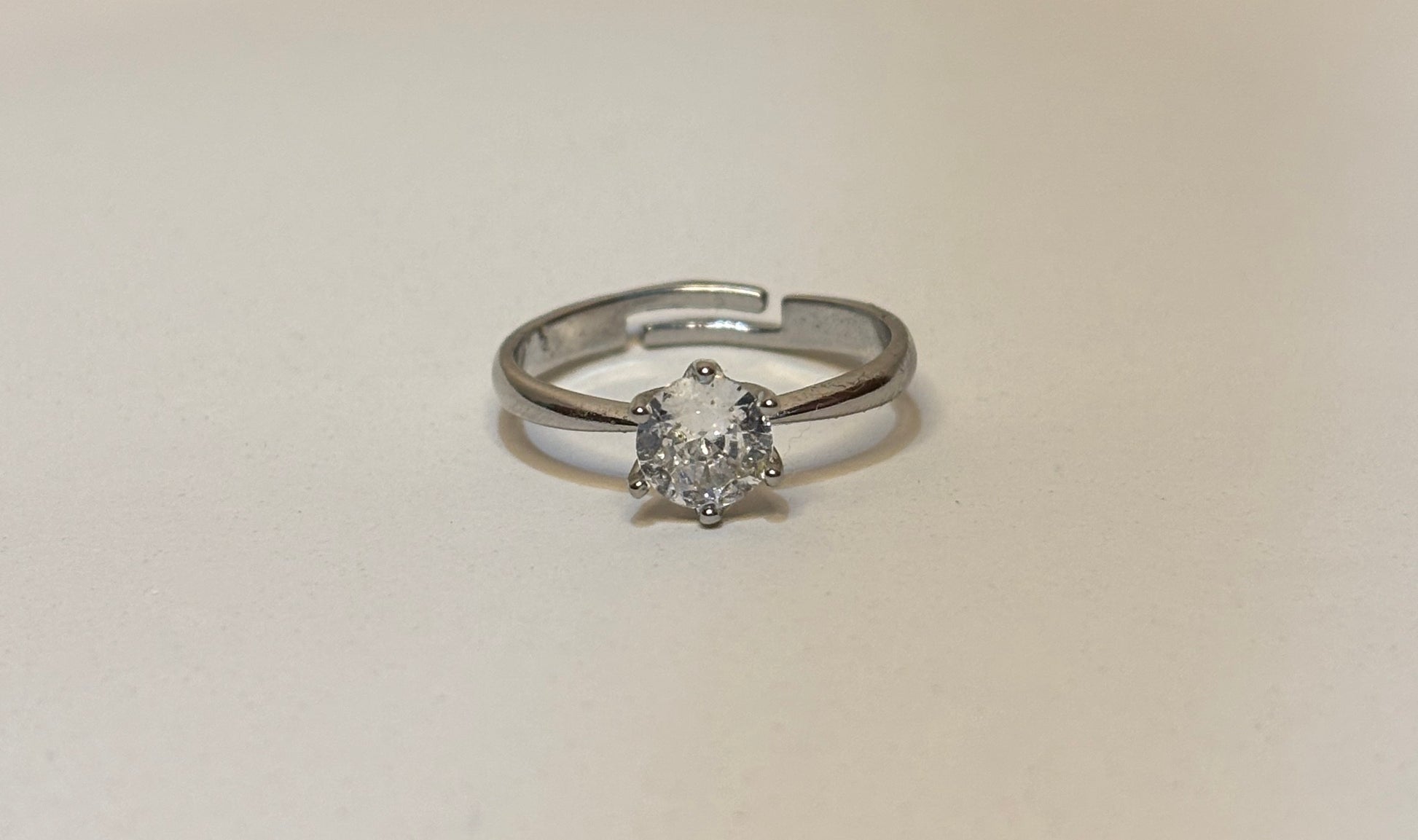 Silver solitaire ring with a diamond on a beige background