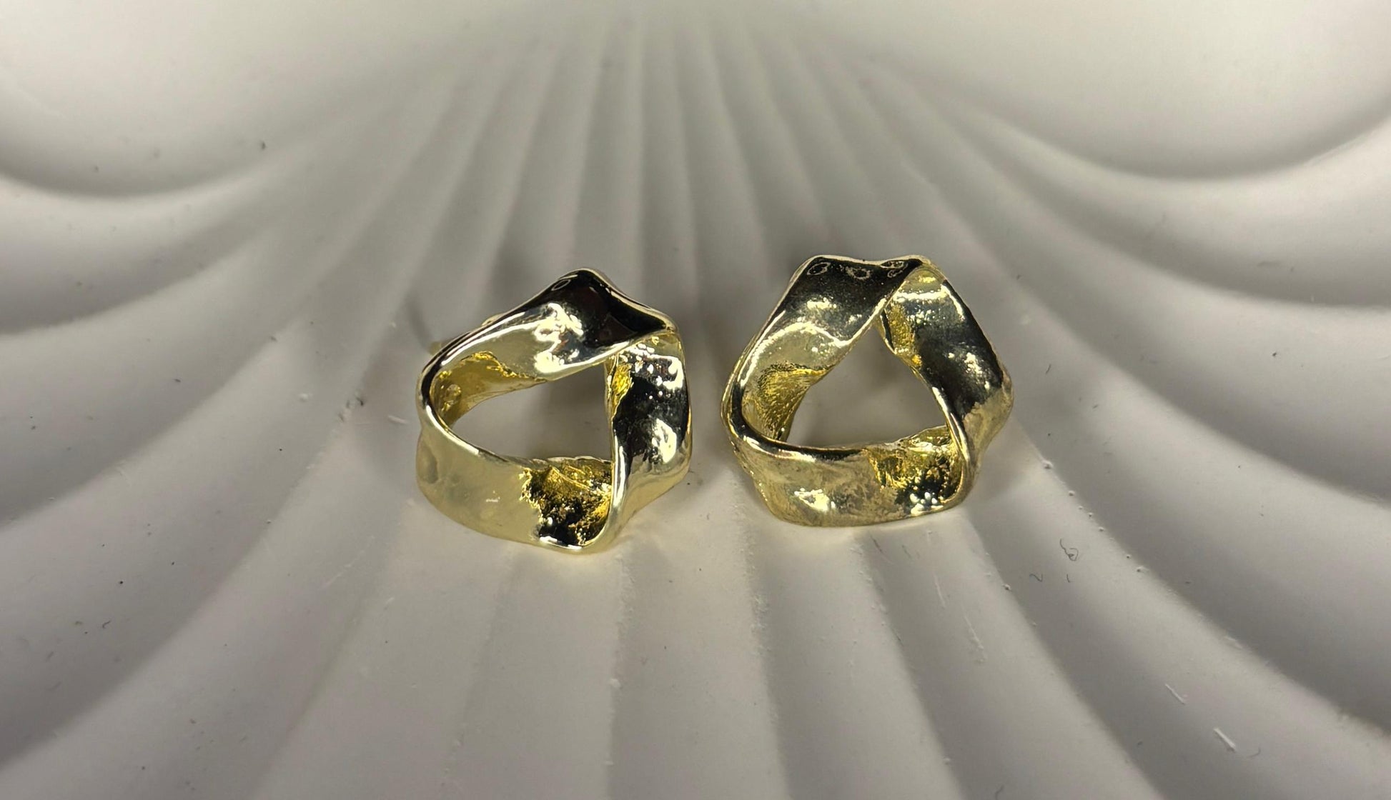 Two gold stud earrings on a textured white surface
