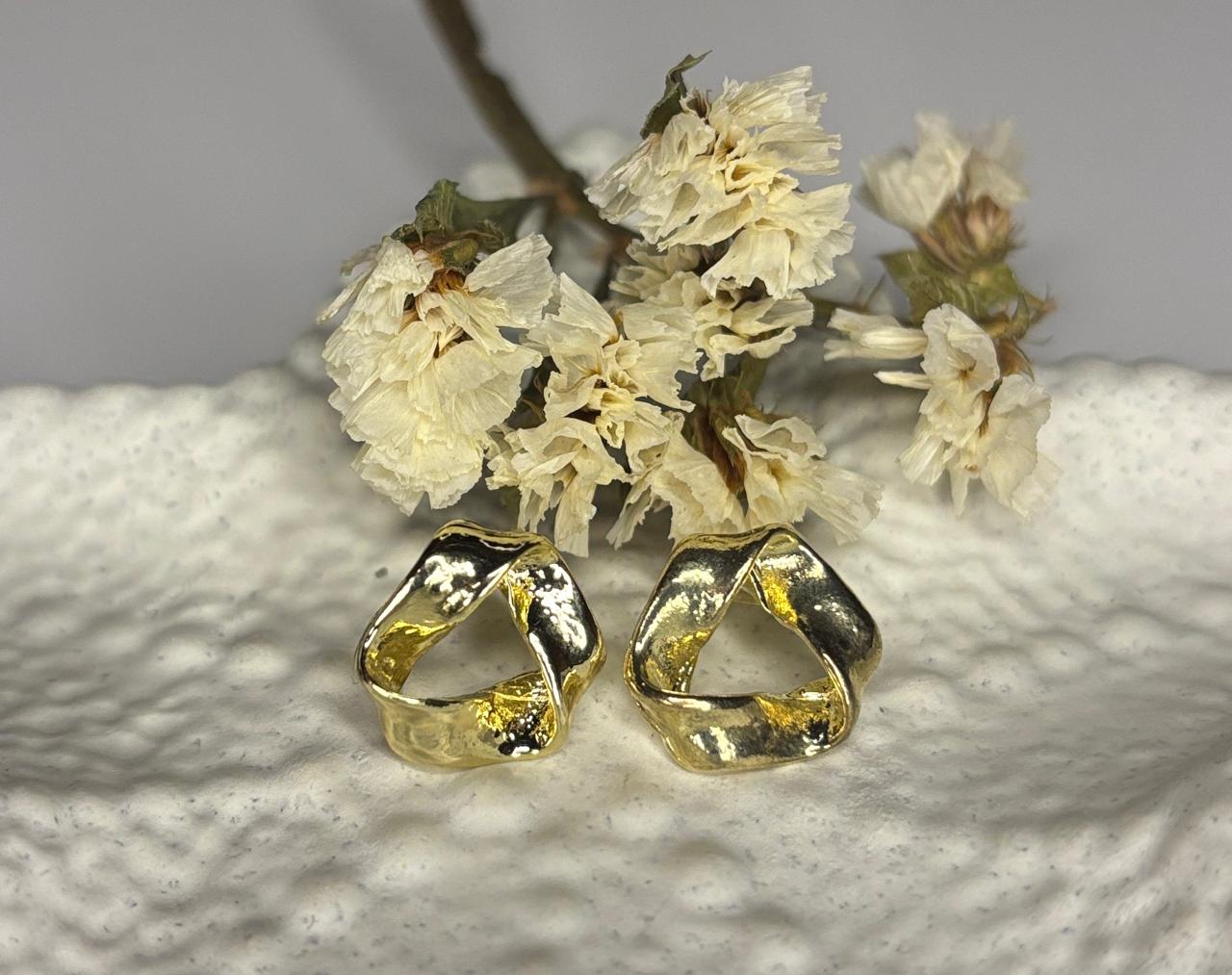 Gold stud earrings on a textured surface with dried flowers