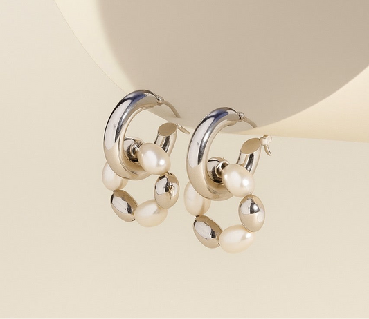Pair of pearl and silver hoop earrings with pearls on a beige background