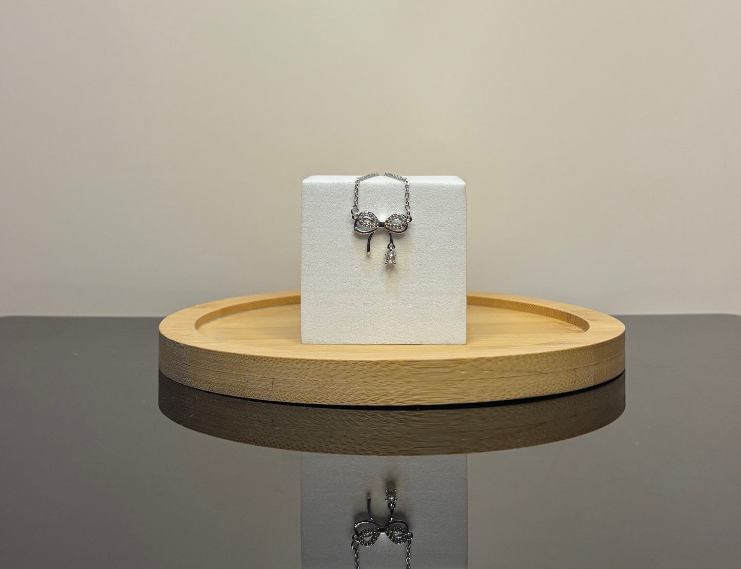 Silver necklace with a bow pendant on a white box on a wooden stand.